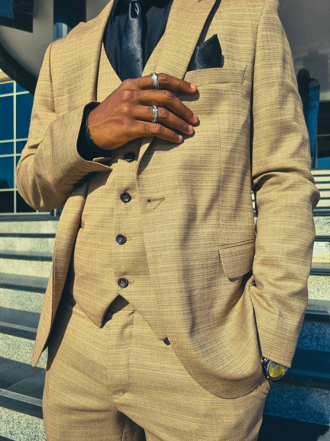 Man in a tan three-piece suit standing outside a modern building.