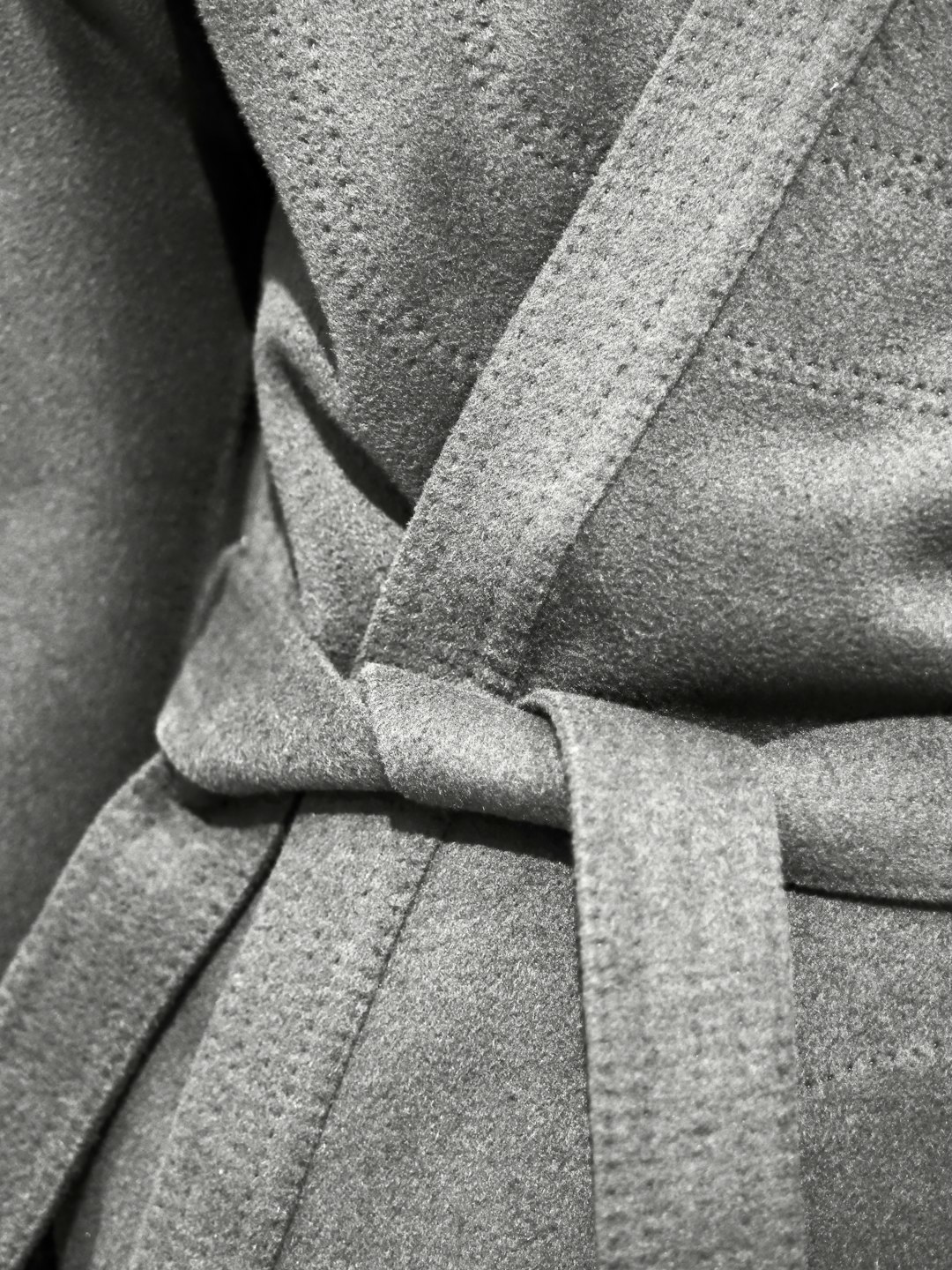 Close up of a grey woolen coat with a belted waist.